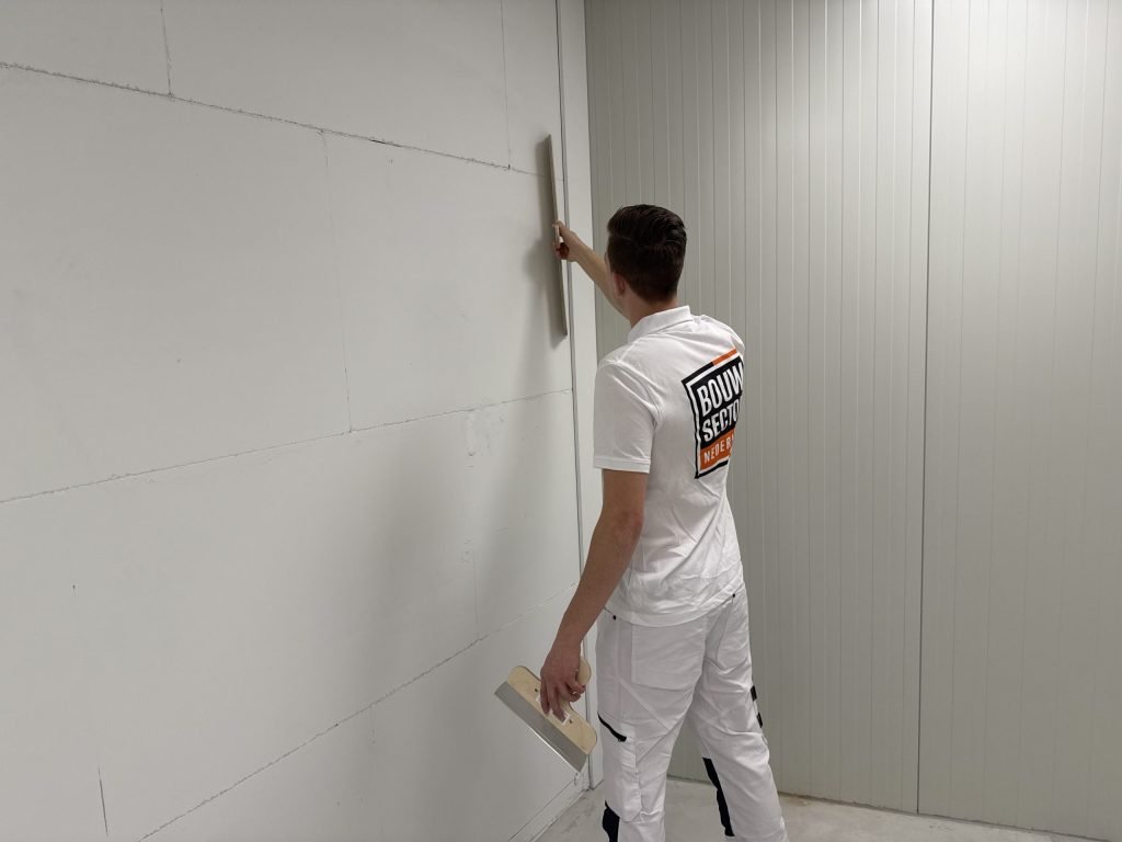 Stukadoor werkt een lange wand af met de spaan omhoog en een plamuurspaan in zijn andere hand