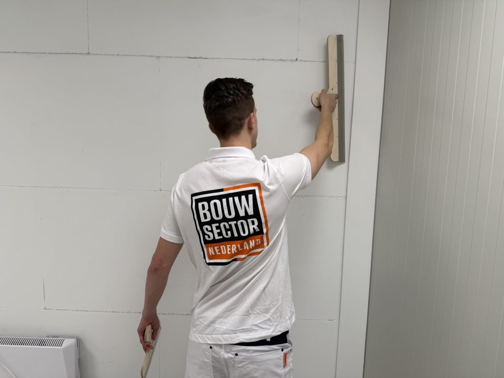 Stukadoor trekt met een lange spaan de bovenkant van een wand van gipsblokken vlak