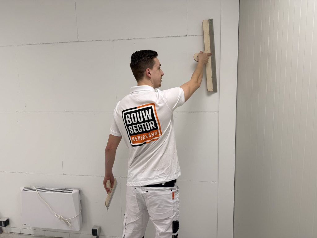 Stukadoor houdt een lange spaan boven zijn hoofd tegen de bovenkant van een wand