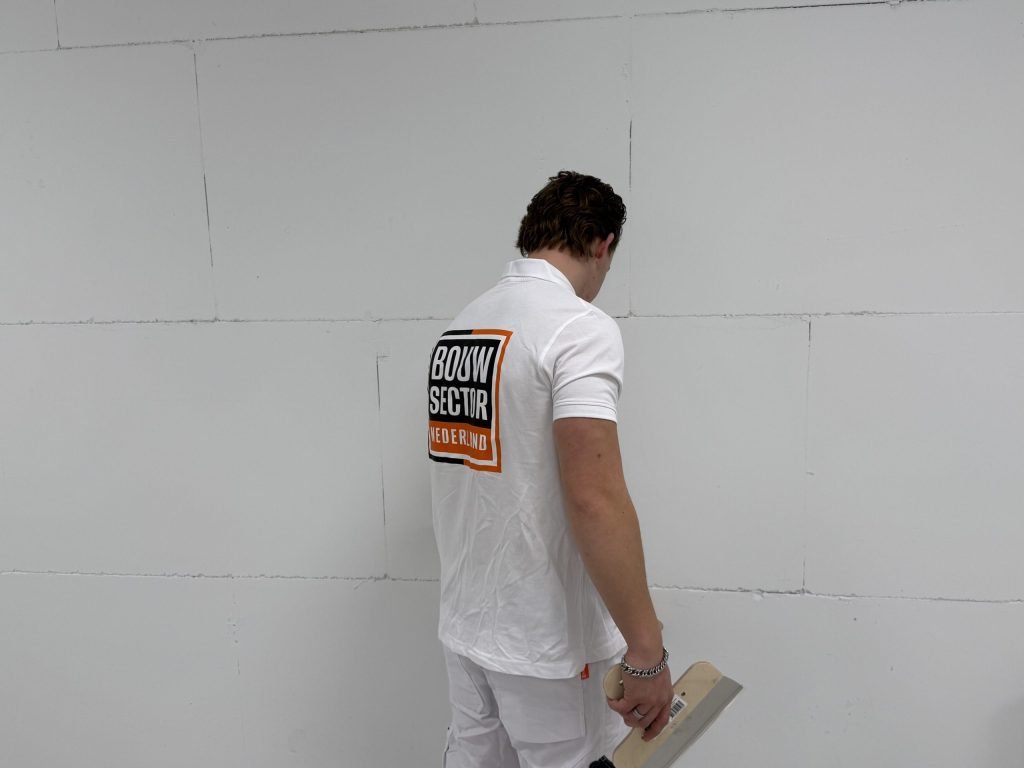 Stukadoor van Bouwsector Nederland met een plakspaan voor een kale wand van gipsblokken met zichtbare voegen